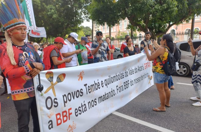 Eine Gruppe von Indigenen protestiert mit einem großen Banner auf einer Straße in einer Stadt: Aufschrift des Banners: Die Völker Tembé und Quilombola des Tales des Acará schreien. BBF tötet uns. BBF raus aus unserem Territorium