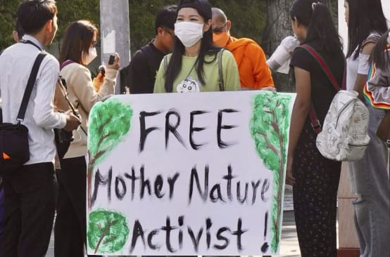 Aktivistin hält großes Plakat in die Kamera mit dem Text „Free Mother Nature Activist!