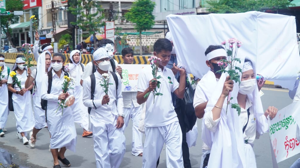 Weiß gekleidete junge Leute laufe mit Blumen in der Hand durch eine Straße in Phnom Penh