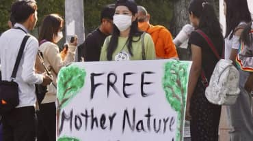 Aktivistin hält großes Plakat in die Kamera mit dem Text „Free Mother Nature Activist!