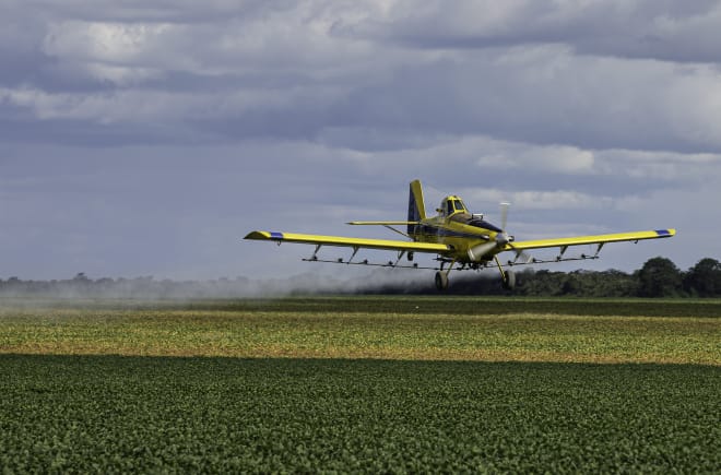 Ein Propellerflugzeug versprüht Pestizide aus der Luft über einem Soja-Feld