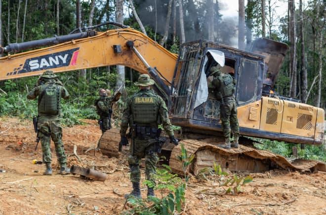Eine Gruppe von Männern in Tarnanzügen der Umweltbehörde IBAMA zerstört einen gelben Bagger im Regenwald