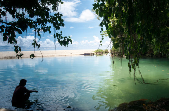 Eine Frau sitzt im Wasser in einer von Felsen und Sandstrand gesäumten Bucht