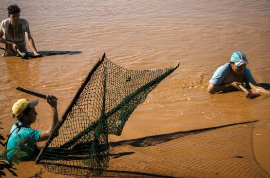 Drei Männer stehen zum Fischfang bis über die Hüften in den braunen Fluten eines Gewässers