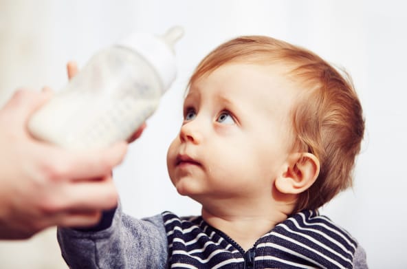 Ein Baby wehrt mit sorgenvollem Blick eine ihm hingehaltene Trinkflasche ab