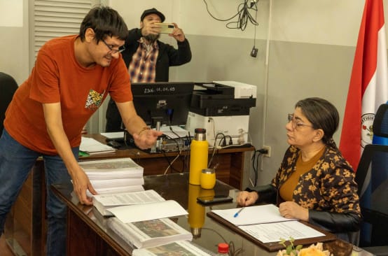 Ein Menschenrechtler übergibt der an ihrem Schreibtisch sitzenden Präsidentin des Indigenen-Instituts die Petition