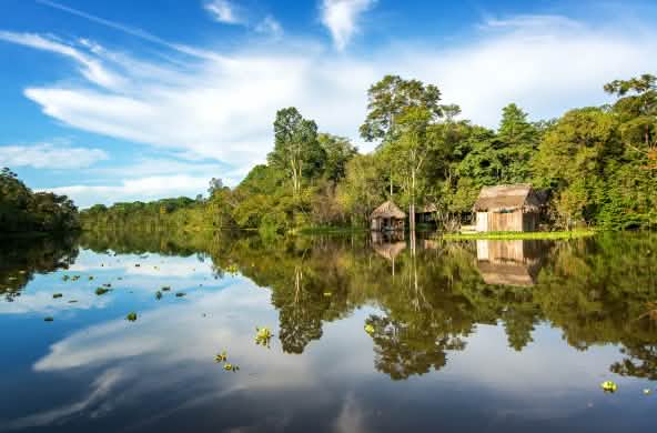 Der Amazonasregenwald und eine Holzhütte spiegeln sich im Wasser des Yanayacu-Flusses in Peru