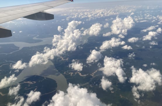 Blick vom Flugzeugfenster auf Wolken, Flüsse und Regenwald, oben im Bild der Flugzeugflügel