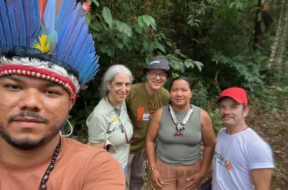 Selfie eines Indigenen mit Federhaube links und dahinter vier Personnen vor Regenwaldvegetation