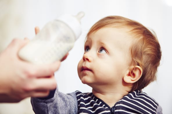 Kleinkind greift nach Babyflasche mit Milch
