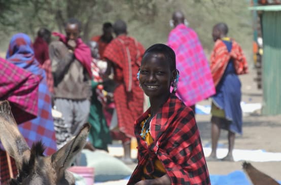 Frauen und Männer der Massai in bunten Tüchern auf einem Markt, eine Frau schaut in die Kamera