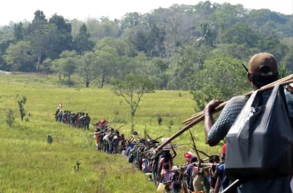 Eine große Gruppe indigene Jäger durchschreitet eine Savanne