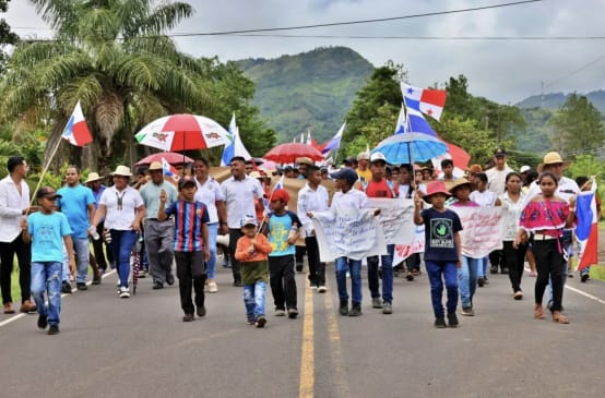Demonstranten marschieren mit Bannern, Landesflaggen und Schirmen auf einer Landstrasse in Panama