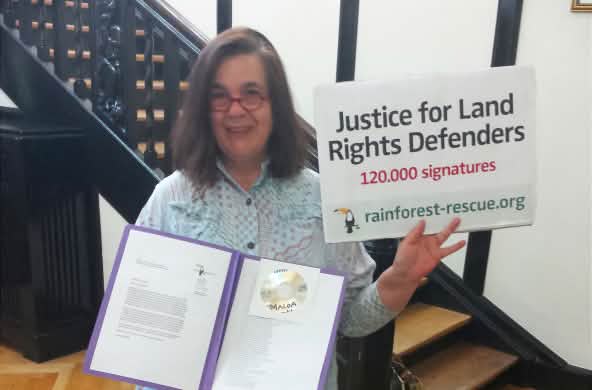 Eine Aktivistin von Rettet den Regenwald hält in der Botschaft von Sierra Leone Petition und Übergabeplakat in die Höhe.