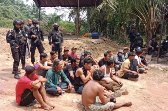 verhaftetete Dayak sitzen auf dem Boden, dahinter bewaffnete Polizisten