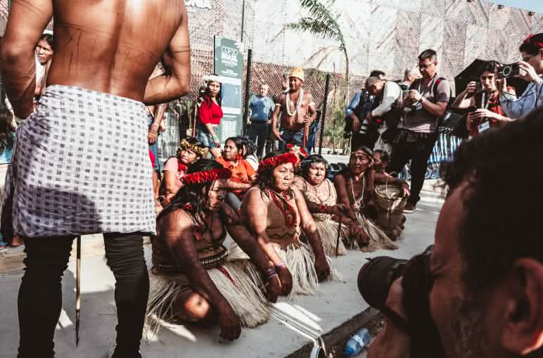 Indigene Frauen blockieren sitzend auf dem Boden den Eingang zur COP30 in Belém