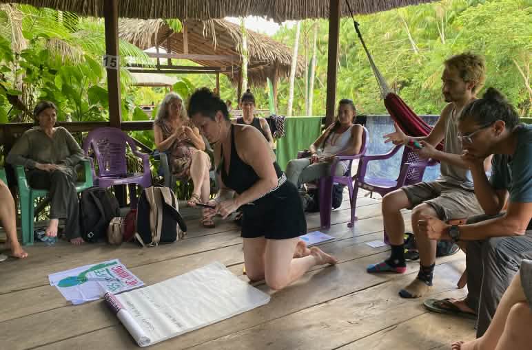 Eine Gruppe von acht Personen auf einem Planungsmeeting in einer offenen Holzhütte im Regenwald