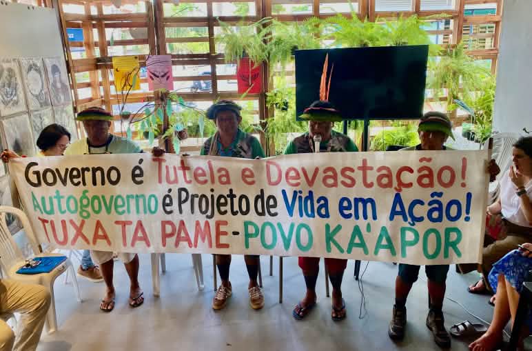 Vier indigene Kaápor halten in einem Sitzungsraum ein beschriftetes Transparent hoch