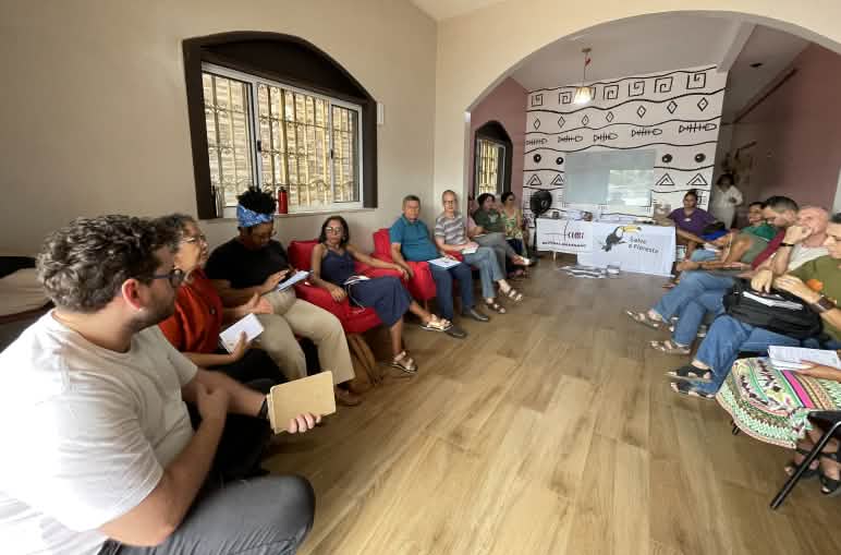 Eine Gruppe von Personen sitzt auf Stühlen in einem Halbkreis in einem Versammlungsraum