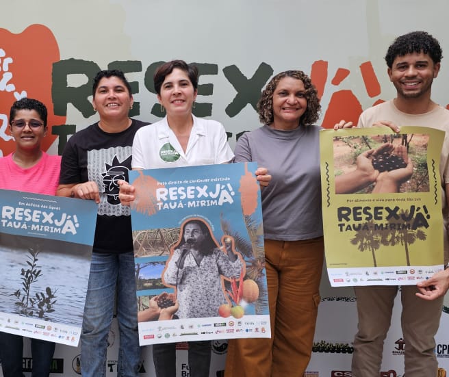 Sechs Personen halten Plakate mit verschiedenen Motiven und der Aufschrift "Resex Tauá-Mirim jetzt!" hoch.
