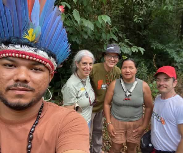 Selfie eines Indigenen mit Federhaube links und dahinter vier Personnen vor Regenwaldvegetation