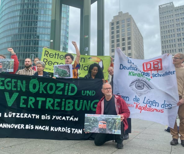 Eine Gruppe von Personen protestiert mit grossen farbigen Bannern vor drei Bürohochhäusern
