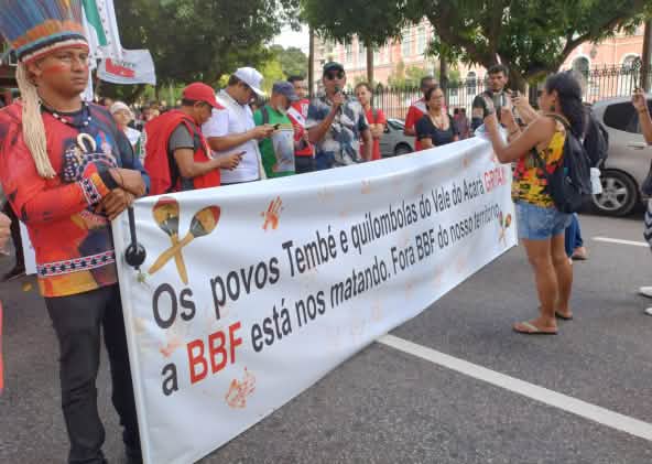 Eine Gruppe von Indigenen protestiert mit einem großen Banner auf einer Straße in einer Stadt: Aufschrift des Banners: Die Völker Tembé und Quilombola des Tales des Acará schreien. BBF tötet uns. BBF raus aus unserem Territorium