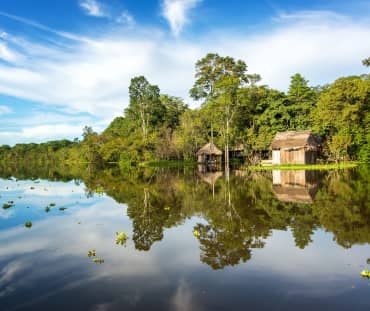 Der Amazonasregenwald und eine Holzhütte spiegeln sich im Wasser des Yanayacu-Flusses in Peru