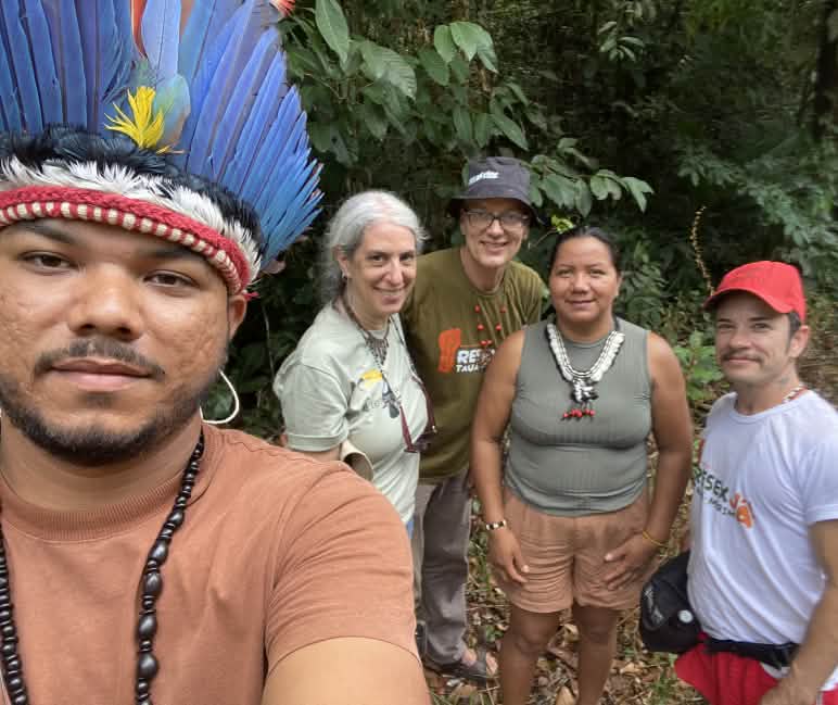 Selfie eines Indigenen mit Federhaube links und dahinter vier Personen vor Regenwaldvegetation