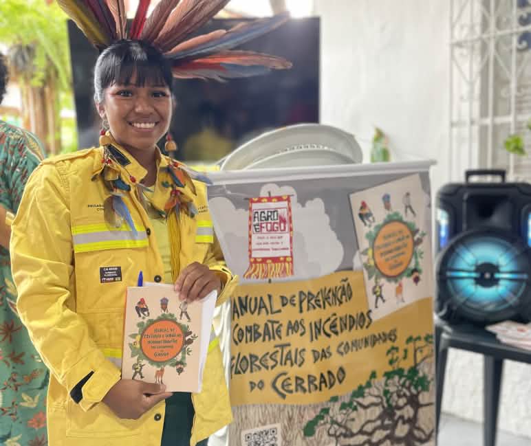 Die junge indigene Frau Fabiana Martins mit Feuerwehrjacke und einem Handbuch von Agro é Fogo zur Brandbekämpfung in den Händen