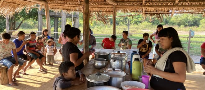 Indigene Frauen, Kinder und Jugendliche beim gemeinschaftlichen Essen in einer offenen Hütte
