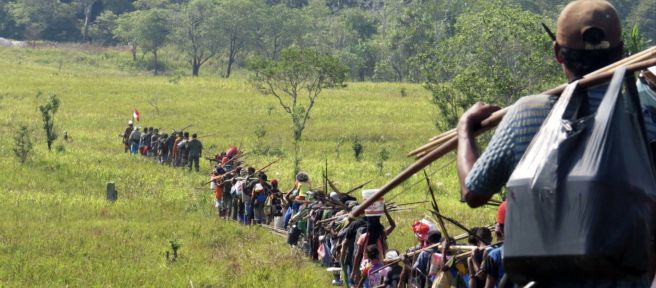 Eine große Gruppe indigene Jäger durchschreitet eine Savanne