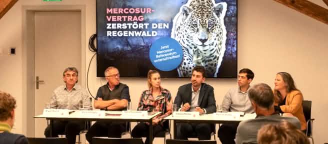 6 Personen bei Pressekonferenz, Banner mit "Mercosur-Vertrag zerstört den Regenwald"