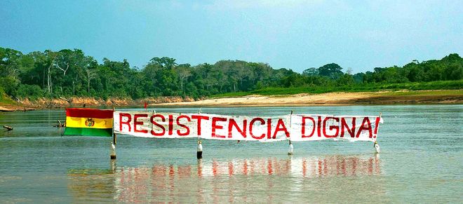 Protestbanner auf einem Fluss im Regenwald von Bolivien: Widerstand bedeutet Würde steht auf dem Banner neben der Flagge Boliviens zu lesen