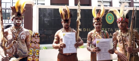 Indigene aus Papua: "Wir gehen in Berufung! Der Prozess entscheidet über die Zukunft des Waldes im Süden Papuas." (© Pusaka) vier Papua in traditioneller Kleidung vor Gerichtsgebäude