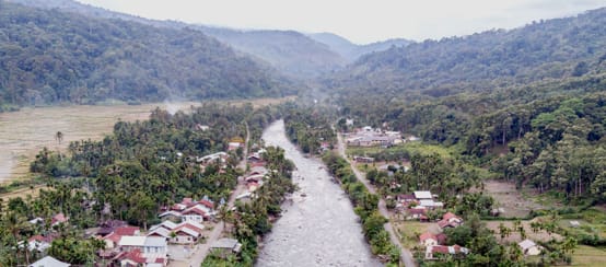 Fluss durch Dorf, im Hintergrund Berge