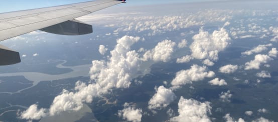 Blick vom Flugzeugfenster auf Wolken, Flüsse und Regenwald, oben im Bild der Flugzeugflügel