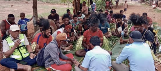 eine Gruppe Papua sitzt auf Palmblättern