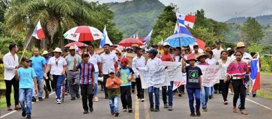 Demonstranten marschieren mit Bannern, Landesflaggen und Schirmen auf einer Landstrasse in Panama