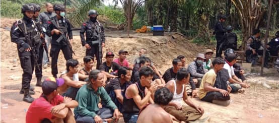 verhaftetete Dayak sitzen auf dem Boden, dahinter bewaffnete Polizisten