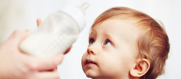 Kleinkind greift nach Babyflasche mit Milch