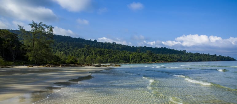 Glasklares Meer, Tieflandregenwälder, Mangroven und artenreiche Tierwelt prägen die Insel Koh Kong. In einer Lagune überspülen Wellen einen Strand, im Hintergrund Wald