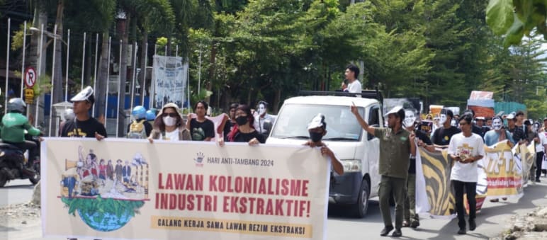Demo, vorne Banner "Gegen den Kolonialismus der extraktiven Industrien", dahinter Menschen und ein Lastwagen