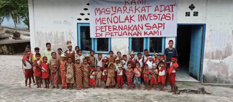 Kinder vor Schule mit Banner "Wir Indigenen lehnen Investitionen in Rinderzucht auf unserem Indigenenland ab"