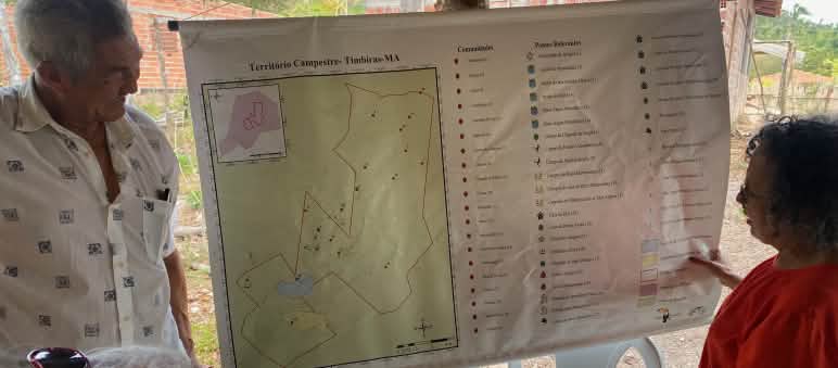 Drei Personen betrachten eine an einem Holzpfosten aufgehängte Landkarte