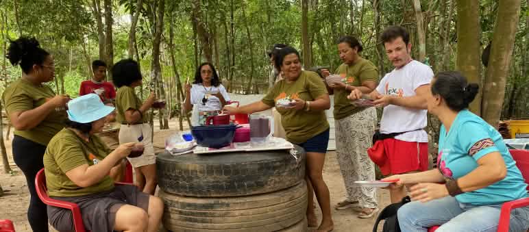 Eine Gruppe von 9 Personen beim Mittagessen und Gespräch um einen improvisierten Tisch herum