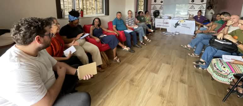 Eine Gruppe von Personen sitzt auf Stühlen in einem Halbkreis in einem Versammlungsraum