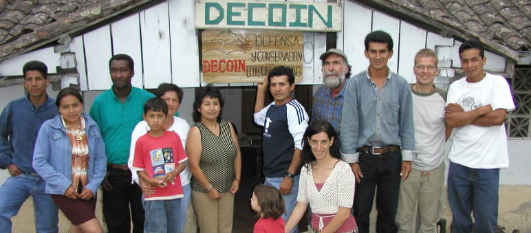 Gruppe von Personen von DECOIN und Rettet den Regenwald vor einer Holzhütte mit der Aufschrift DECOIN
