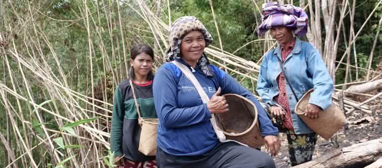 drei Dayak-Frauen mit Körben zum Sammeln lächeln in die Kamera.