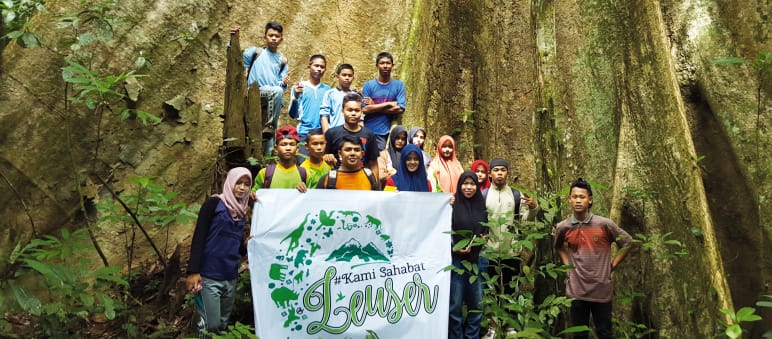 „Wir sind Freunde von Leuser“ steht auf dem Plakat der von Rudi Putra ins Leben gerufenen Jugendbewegung. Der Urwaldriese in ihrem Rücken zeigt, was es zu schützen gilt. Er wächst im Leuser Nationalpark Widerstand im Leuser Nationalpark